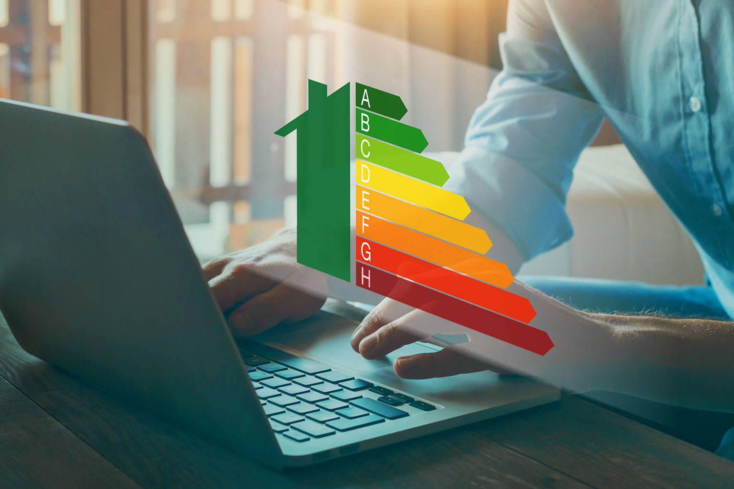 Eine Person tippt auf einem Laptop. Darüber ist ein farbiger Energieeffizienz-Pfeildiagramm in Form eines Hauses eingeblendet, das von grün (A, sehr effizient) bis dunkelrot (H, wenig effizient) reicht.